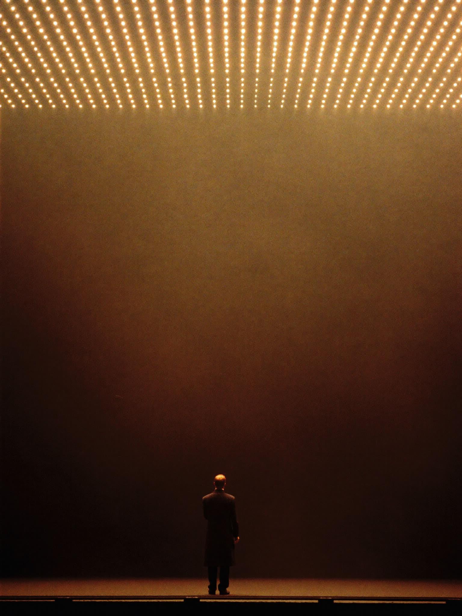 A promoter silhouetted at the edge of a stage above a glowing crowd